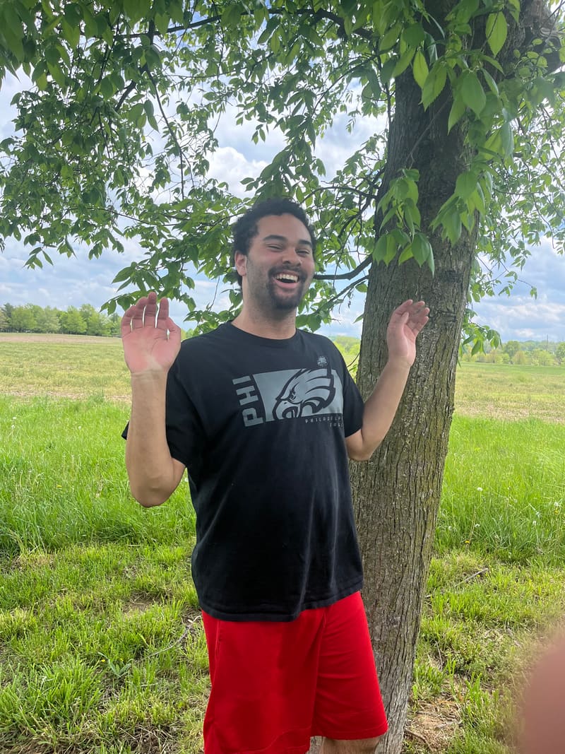 PAAL student Tristan outdoors in the community, smiling by a tree